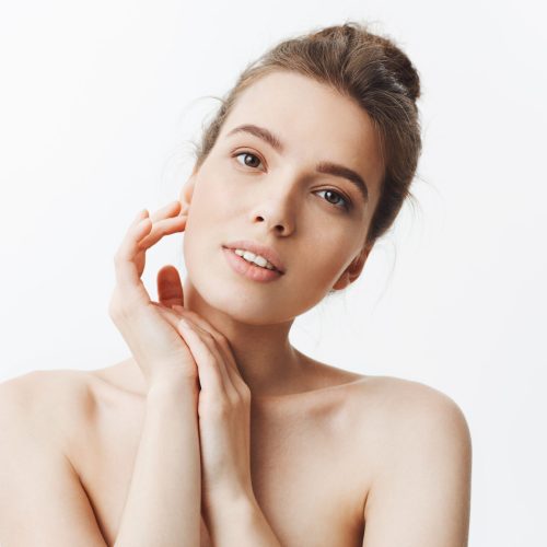 Beauty and health. Young good-looking skinny caucasian girl with dark hair in bun hairstyle being naked, looking in camera with relaxed and happy expression, touching hand with hands, feeling refreshed after spa treatments