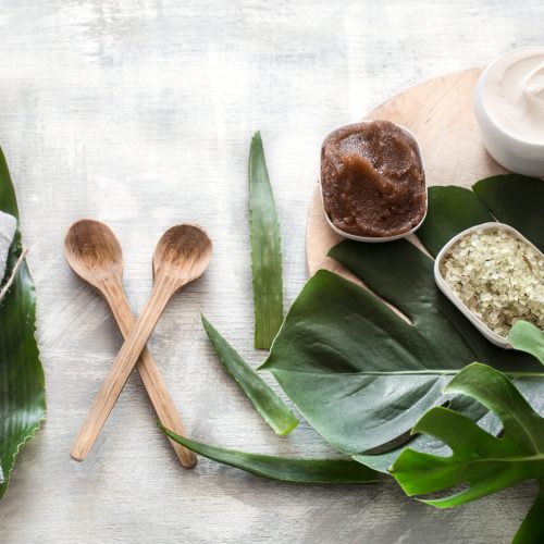 Flat-lay natural cosmetics and accessories with tropical leaves to cleanse the skin. Basic hygiene and body care items on white background, copy space.