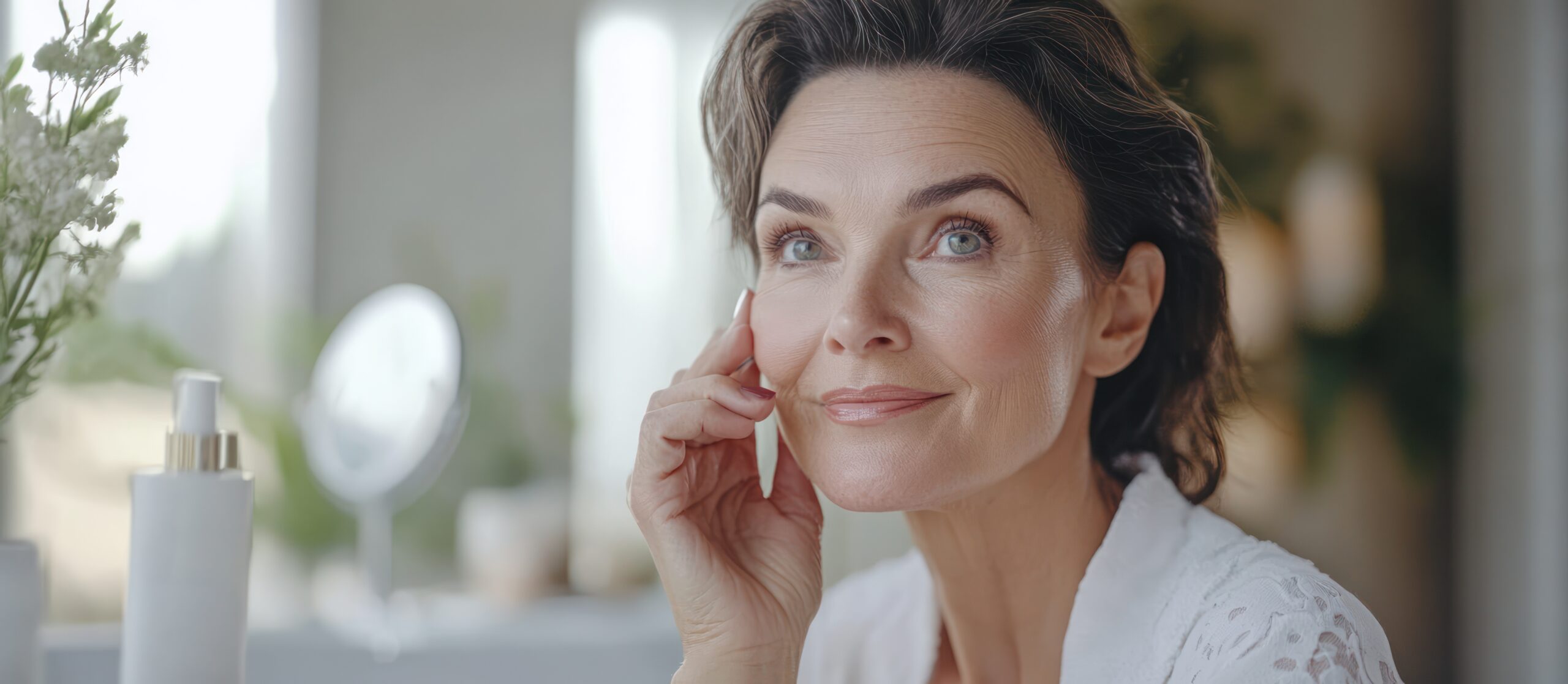 Beautiful mature woman looking away thoughtfully with her hand on her face, standing in a bright room.